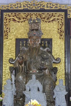 A deity seated majestically on a throne, Shou Xing (also known as Shou Lao or Nanji Xianweng), the god of longevity, carved from dark wood with gold inlays, surrounded by dragon motifs and cloud patterns, symbolises wisdom and long life in Chinese-Daoist culture, Chee Chin Khor Temple, Bangkok, Thailand