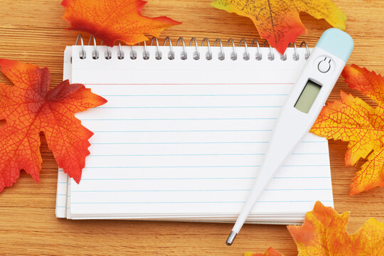 Fall leaves with a blank notepad with thermometer on wood for your autumn illness