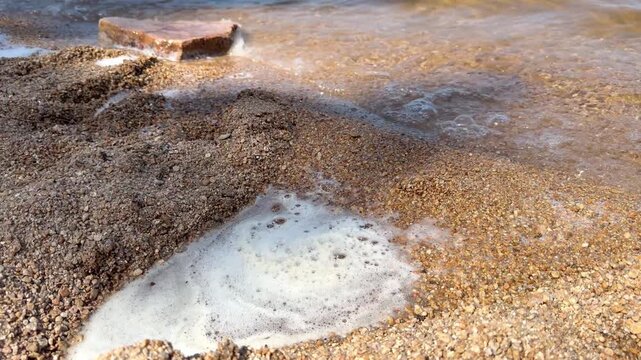 4K video of small foamy waves washing over a pebble shore in Borovoe, Burabay, Kazakhstan. Close view of moving lake water, wet stones and natural shoreline texture.