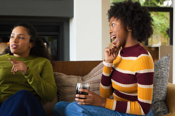 Fototapeta premium African American women friends chatting on sofa in living room, holding stemless glass, copy space