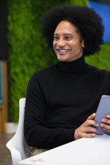 African American man in black turtleneck smiling and holding tablet at office table near green wall © WavebreakMediaMicro