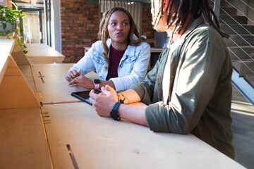 African American colleagues discussing project on tablet at communal table with watches and jackets © WavebreakMediaMicro