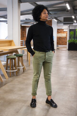 African American man standing hands in pockets, wearing black turtleneck by wooden communal table © WavebreakMediaMicro