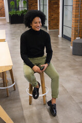 Man sitting on wooden bar stool in co-working lounge wearing black turtleneck, holding smartphone © WavebreakMediaMicro