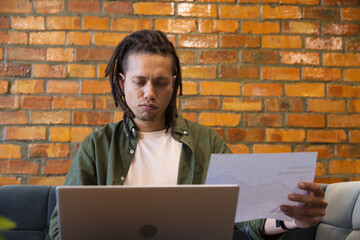 African American man wearing green shirt reviewing chart while working on laptop against brick wall © WavebreakMediaMicro