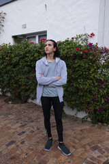 Adult man standing on brickway by white plaster wall with bougainvillea hedge in hoodie sneakers © WavebreakMediaMicro
