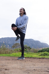 African American man stretching balancing on one leg on trail wearing gray hoodie and olive shoes © WavebreakMediaMicro