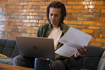 Adult African American man reviewing charts while checking laptop in cafe lounge on tufted sofa © WavebreakMediaMicro