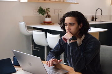 African American man working on laptop at kitchen table wearing headphones checking watch © WavebreakMediaMicro
