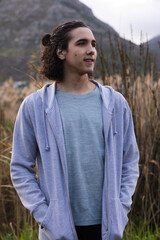 African-American man 20s standing waist-deep in reeds by foothill wearing grey hoodie, blue tee © WavebreakMediaMicro