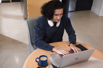 African American man wearing dark knit sweater working on laptop at home with headphones and mug © WavebreakMediaMicro