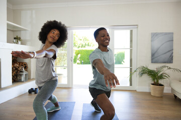 Fototapeta premium African American couple doing forward lunges on dark mats in bright living room by sliding doors
