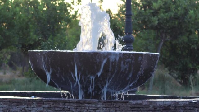 Water overflowing dark bowl fountain in park in Marrakech, Morocco
