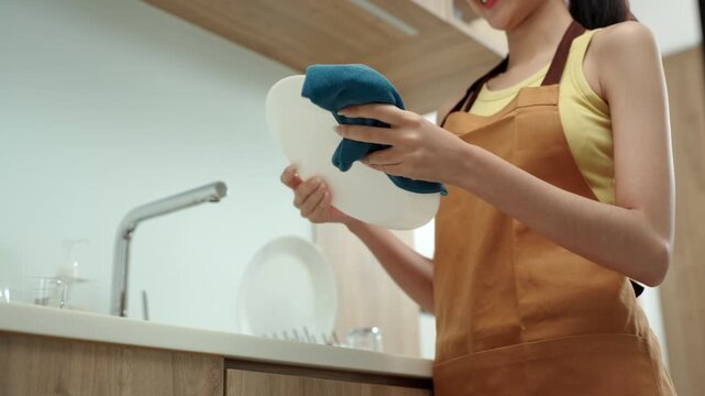 Close-up Happy housewife carefully drying clean dishes at the kitchen sink after washing. Household chores, kitchen hygiene, home care and everyday domestic life.
