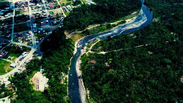 Drone footage looks across dense rainforest in Ecuador&rsquo;s Oriente, where a winding river with pale sandy banks cuts through a vast green forest canopy. Cloud shadows cross the landscape beneath a cloud