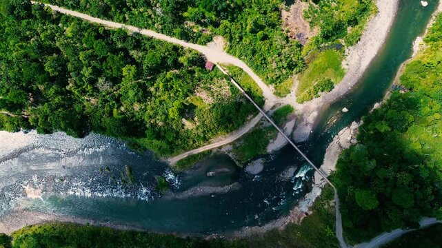A winding river and pale gravel bars cut through dense green rainforest, with a narrow bridge and forest tracks nearby. Roads and buildings in a small settlement meet the forest edge in Ecuador&rsquo;s Orie