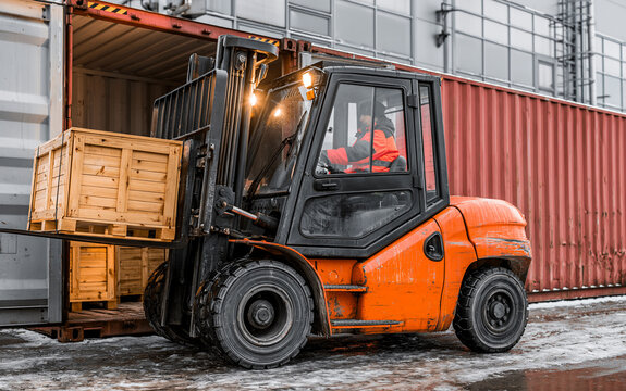 Orange forklift loading wooden crates into shipping container