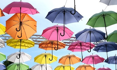 Colorful umbrellas hanging upside down in the sky above a street, pink, orange, yellow, blue and green, summer decoration Many multicolored open umbrellas suspended in the air as an out © Anna
