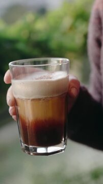 Woman gently holding a glass of homemade pumpkin spice latte in warm autumn sunlight. Cozy seasonal lifestyle footage with subtle hand movements