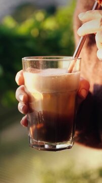 Woman drinking homemade pumpkin spice latte through a straw while holding the glass in warm golden autumn sunlight. Cozy seasonal lifestyle footage with creamy foam