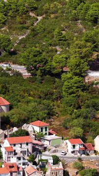 Croatia, aerial footage of a coastal road winding through dense pine tree forests and traditional stone houses