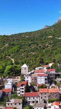Croatia, aerial view of a small coastal village with traditional red roof houses and mountains in the background