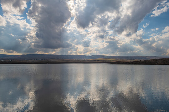 Scenic view of Alankoz pond with reflection of dramatic cloudy sky and sunbeams. Located between Karacadag town and Kirkkoyun village in Diyarbakir, Turkey. Beautiful natural volcanic landscape.