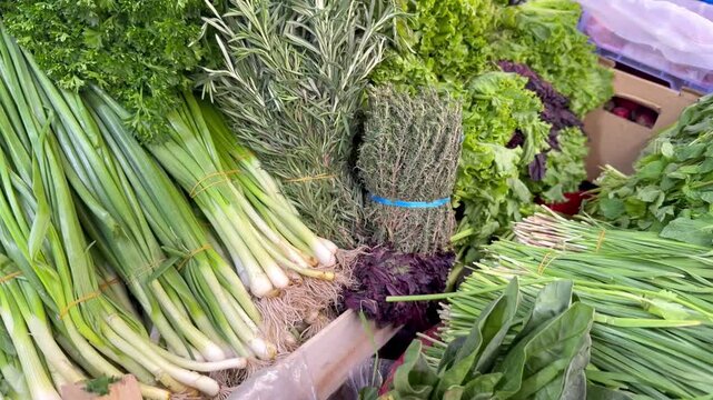 4K video of fresh green herbs and leafy vegetables displayed for sale at a local food market. Bundles of spring onions, dill and assorted greens create a vibrant scene of fresh natural produce and hea