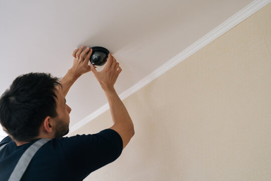 Professional worker hands installing modern dome security camera on ceiling, ensuring full monitoring and protection for residential or commercial property safety.
