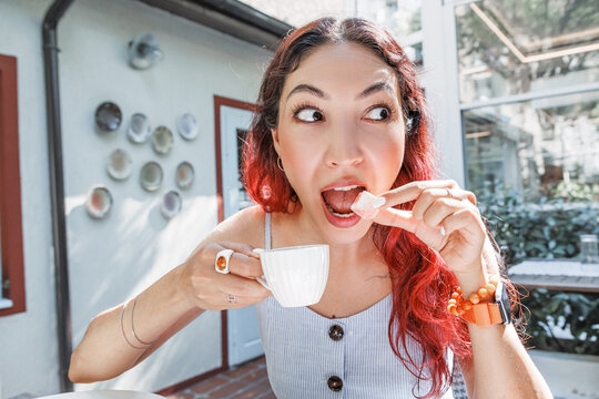 Outdoor cafe terrace setting: woman eating lokum with expressive face, holding small espresso cup. Food and lifestyle concept.