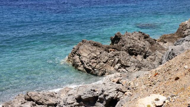 Powerful sea waves roll onto a rugged rocky shore, creating dynamic splashes and foamy patterns along the coastline. Ocean water crashes against weathered stones as the surf moves rhythmically