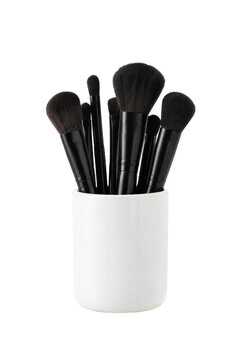 Collection of black makeup brushes with soft bristles stands upright in a white ceramic holder against a clean white background