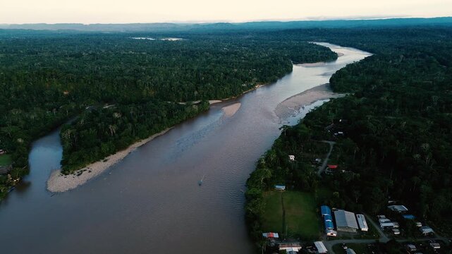 A broad brown river curves through dense tropical rainforest near Misahualli, Ecuador, with exposed sandbars, small boats along the banks and a settlement among the trees. The aerial view takes in the
