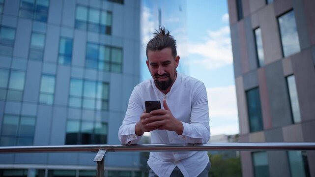 A smiling business man leans on a railing while checking his smartphone, then lifts it to his ear and starts a phone conversation.