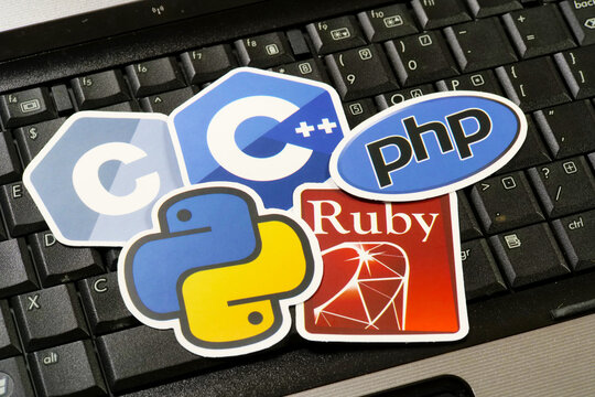 Five programming language logo stickers on a black laptop keyboard: C, C++, PHP, Python and Ruby, closeup of developer laptop with coding language decals, software development and programming concept