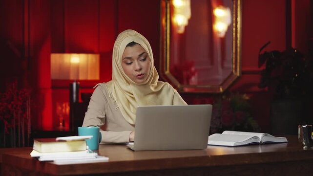 Young Muslim woman in hijab giving online video lesson on laptop at home