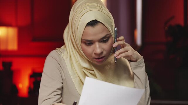 Busy Middle Eastern woman typing on laptop and discussing work by phone