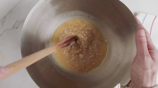 Hands of a woman stirring ingredients with a wooden spoon. 