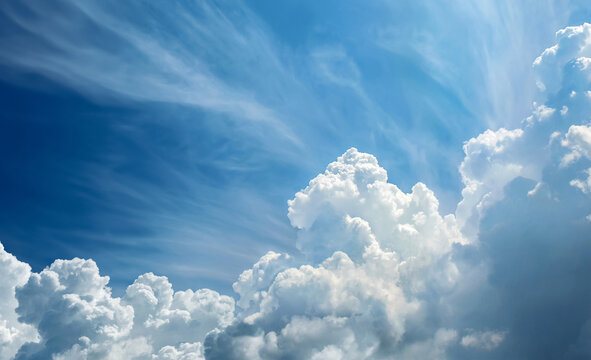Bright blue sky with large white cumulus clouds and soft cirrus streaks, illuminated by natural daylight. The image represents calm weather, atmospheric beauty, and a peaceful natural background.