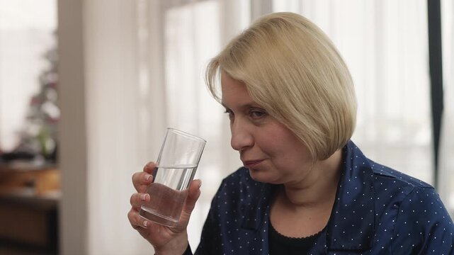 Happy woman in her 50s takes vitamin with water as part of morning routine