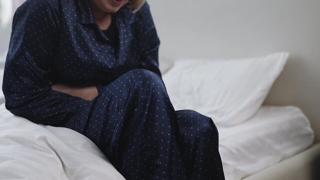 Woman in her 50s feels sharp abdominal pain while sitting on bed, feeling sick