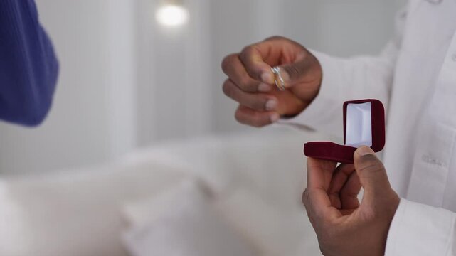 Young African American man proposes to girlfriend, putting ring on her finger