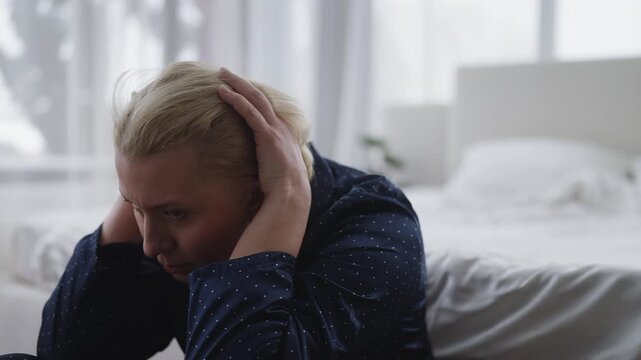 Sad woman in her 50s sits on bedroom floor alone, feeling lonely and crying