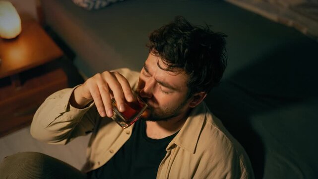 Alcoholism crisis forces lonely adult male to drink whiskey on carpet. Acute emotional suffering