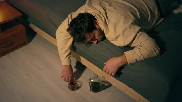 Intoxicated adult male collapses passed out on bed with liquor on floor. Severe burnout and despair