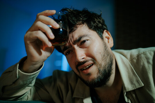 Distressed man drinks alcohol alone on bedroom carpet in acute grief. Personal defeat crisis