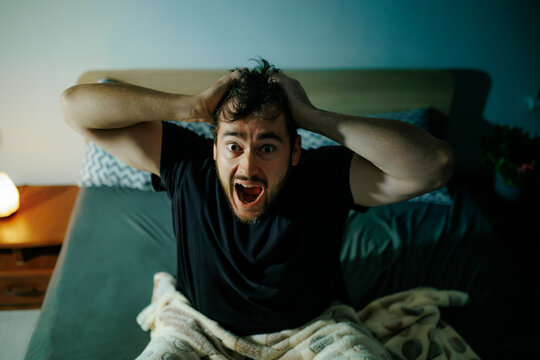 Frightened man sits in gloomy bedroom surviving sleep paralysis and terror. Acute agony crisis