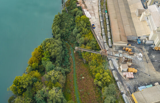 Aerial view of an industrial cement plant beside a river, featuring freight tanker wagons, storage buildings, and bulk material handling infrastructure in France.