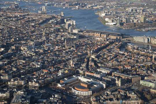 Aerial view of the historic city center of Amsterdam, featuring its iconic canal network, dense urban architecture, and the IJ river waterfront in Amsterdam, North Holland, Netherlands.