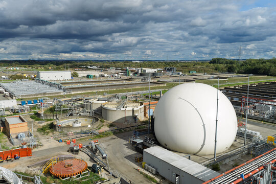Aerial view of a water treatment plant featuring a large white spherical digester tank, circular sedimentation tanks, and industrial infrastructure in the United Kingdom.